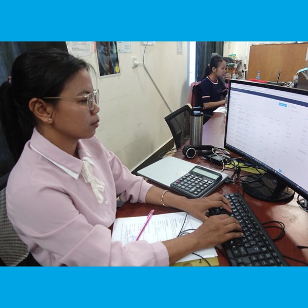 A TukTuk staff member types at a computer, with a calculator and papers beside her