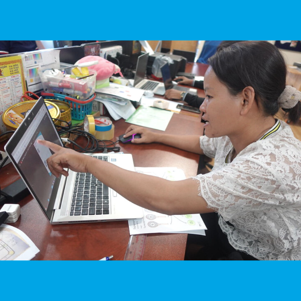 A TukTuk staff member points at a laptop screen while explaining worksheets at her desk