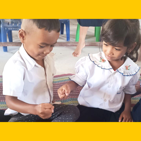 A schoolboy and a schoolgirl sit on a mat in class, looking down at something in their hands