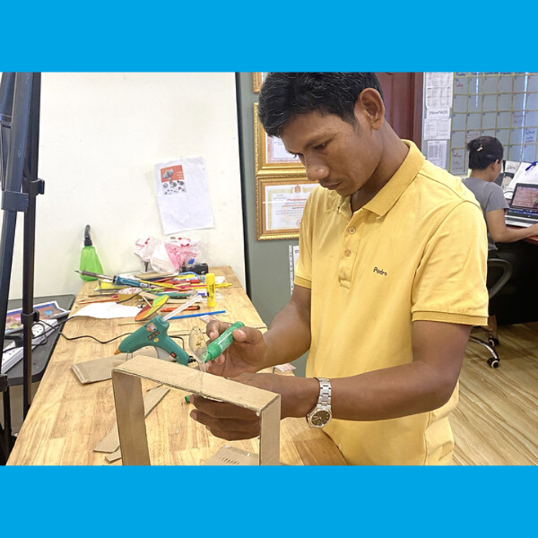 A TukTuk staff member glues a cardboard frame at a craft table in the office