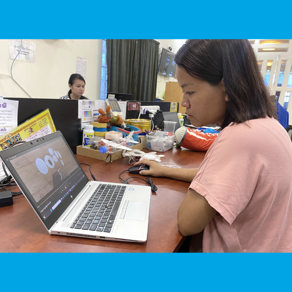 A TukTuk team member works at a laptop on her desk, with craft materials beside her