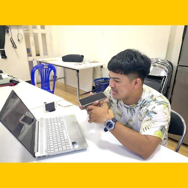 A TukTuk team member talks into a phone beside an open laptop at a table in the office