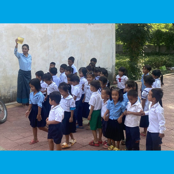 A teacher holds up a card as preschool children in uniforms line up outside a school