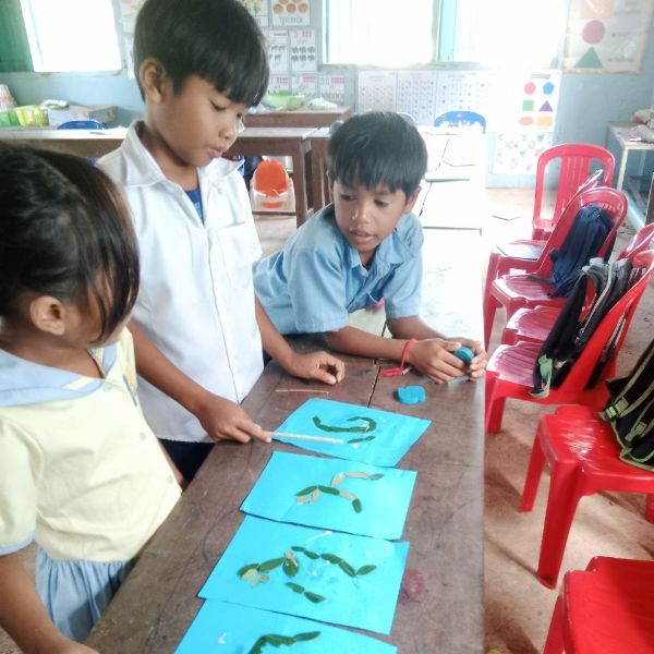 Preschool children make pictures from leaves and modelling clay on blue paper at a classroom table