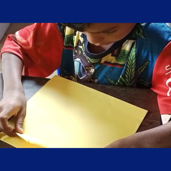 A child's hands fold a sheet of yellow paper at a desk