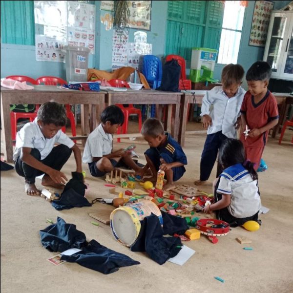 Preschool children play on the classroom floor with wooden blocks, a drum and other toys