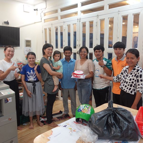 TukTuk staff and visitors gather in the office around a small birthday cake, one holding a toddler