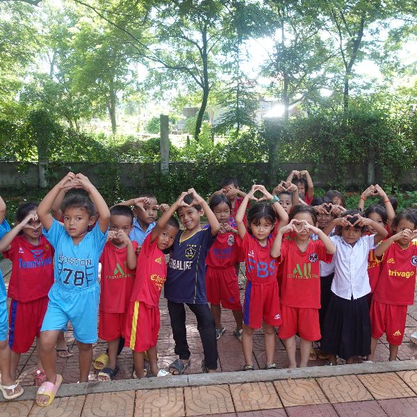 Preschool children in red and blue sports shirts make heart shapes with their hands outdoors