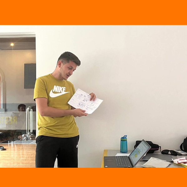 A man holds up a hand-drawn storyboard page beside a laptop in a white room
