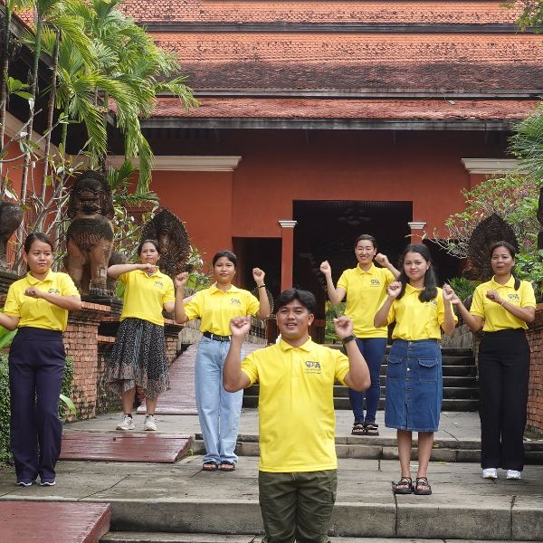 TukTuk staff in yellow shirts pose with raised fists on temple steps in front of a red-walled building