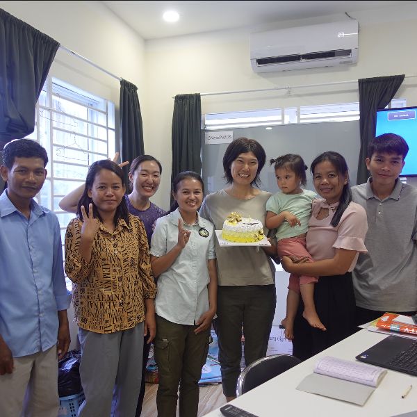 TukTuk staff and friends pose in the office around a small cake, one holding a toddler