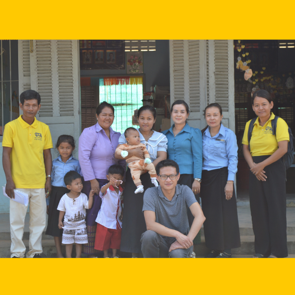 Teachers, TukTuk staff and children pose together in front of a school building