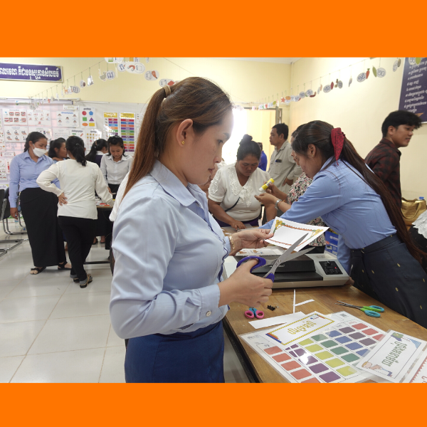 Teachers cut out and laminate classroom decoration sheets in a decorated classroom