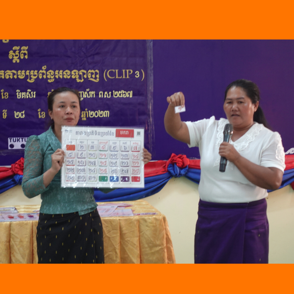 Two women present a card chart at the CLIP3 workshop, one holding it and one speaking into a microphone