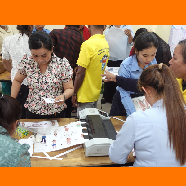 Teachers and a TukTuk staff member work around a laminator, preparing decoration sheets