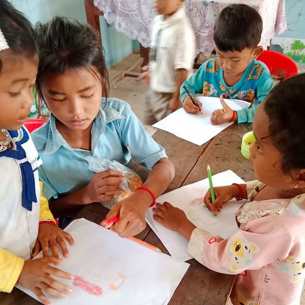 Children draw with coloured pencils on paper at a classroom table
