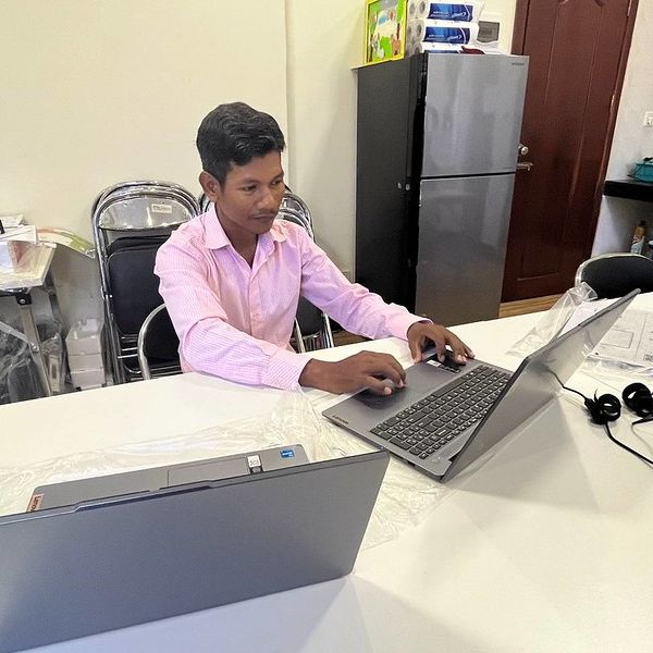 A man in a pink shirt works on a laptop at a white table in the office