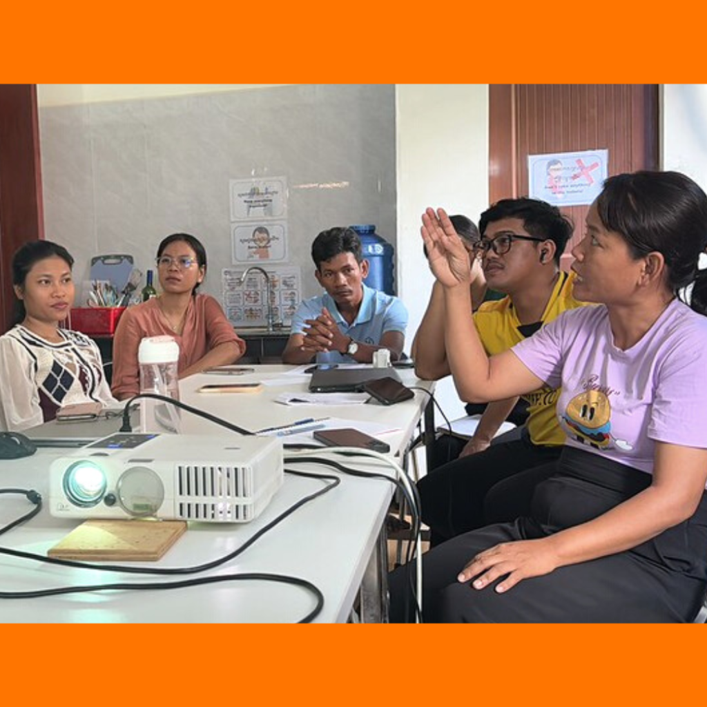 TukTuk staff discuss around a table with a projector, one raising her hand