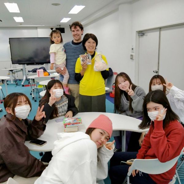 Japanese university students and visitors smile and make peace signs in a classroom