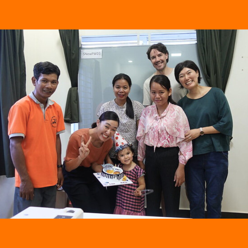 TukTuk staff and visitors gather around a birthday cake, with a toddler in a party hat