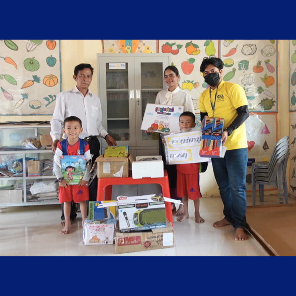 Teachers and a TukTuk staff member hold delivered tools beside two preschool children and a new cabinet