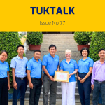 TukTalk 77 cover: TukTuk staff, a visiting Rotary volunteer and a local official hold a framed certificate on steps