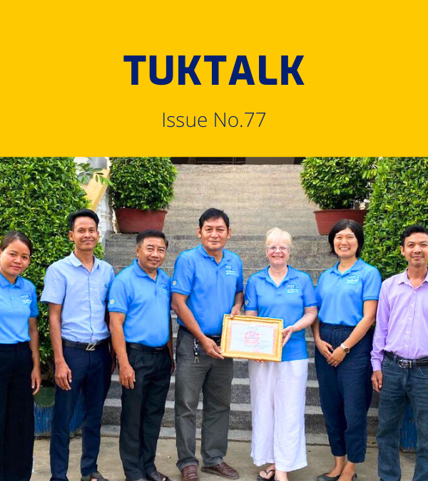 TukTalk 77 cover: TukTuk staff, a visiting Rotary volunteer and a local official hold a framed certificate on steps