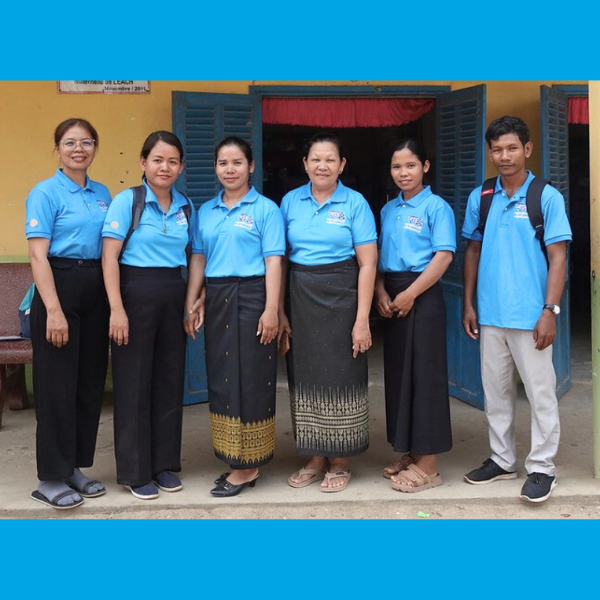 Six people in blue TukTuk polo shirts stand in a row outside a school building