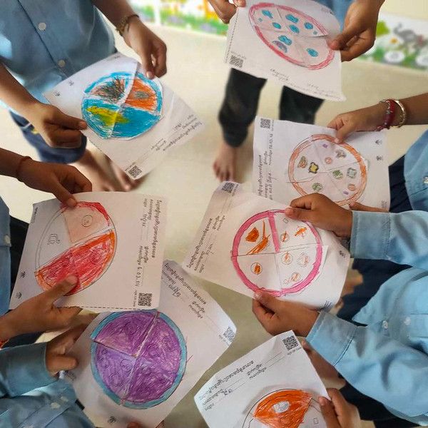 Hands hold colourful round paper worksheets divided into four sections, shown from above in a circle of participants