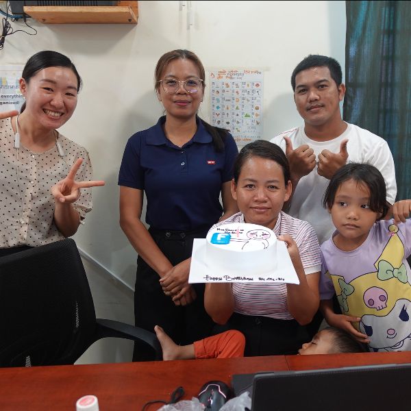 Smiling adults and a young girl pose in an office behind a birthday cake held up for the camera