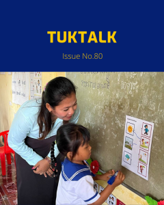 TukTalk 80 cover: a preschool teacher helps a small girl in school uniform match picture cards on a classroom wall