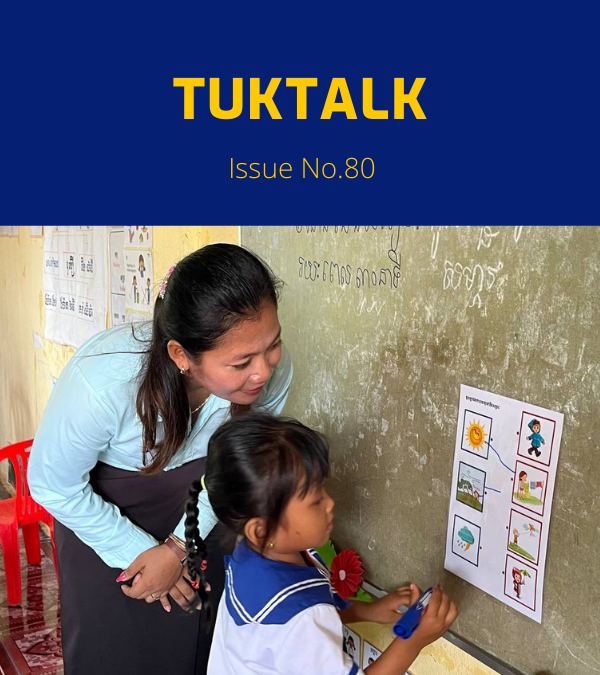TukTalk 80 cover: a preschool teacher helps a small girl in school uniform match picture cards on a classroom wall