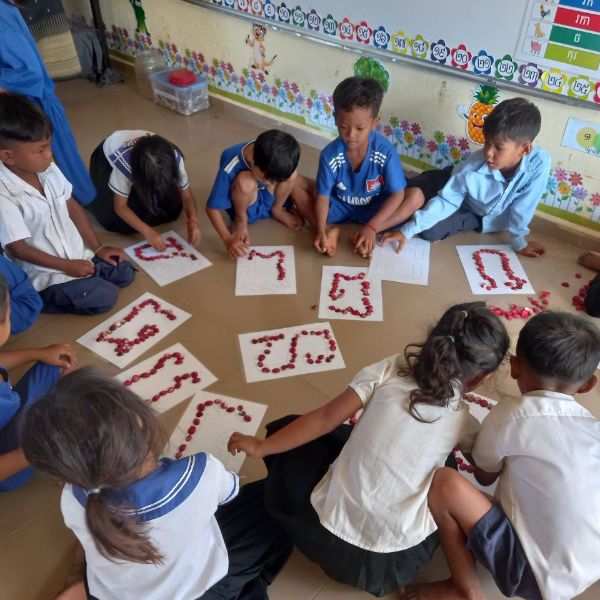 Preschool children kneel on the classroom floor making Khmer letters from small red seeds on paper sheets