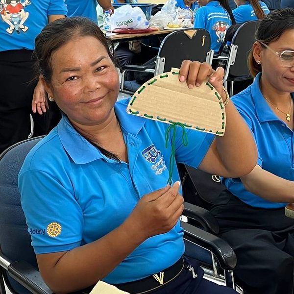 A smiling teacher holds up a cardboard half-circle craft stitched with green yarn at the workshop