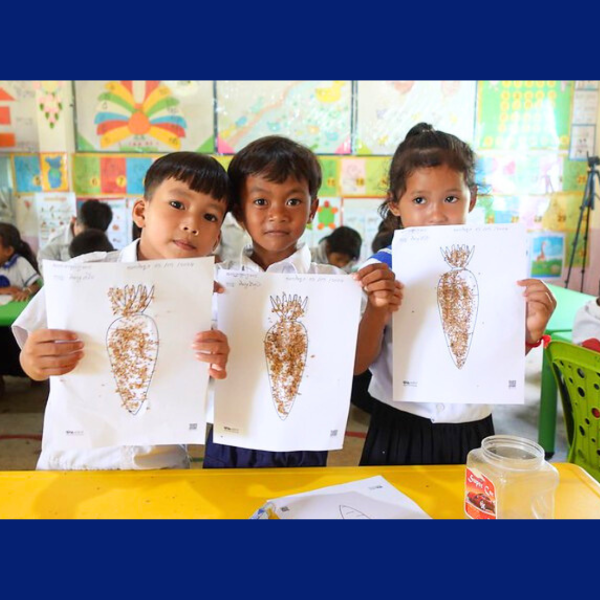 Three children proudly hold up their carrot drawings decorated with seeds in class
