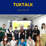 A TukTuk staff member poses with a group of students in front of a TukTuk presentation screen