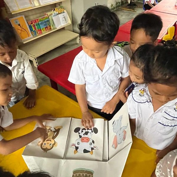 Children gather around a table and point at animal picture cards showing a monkey, a cow and an elephant