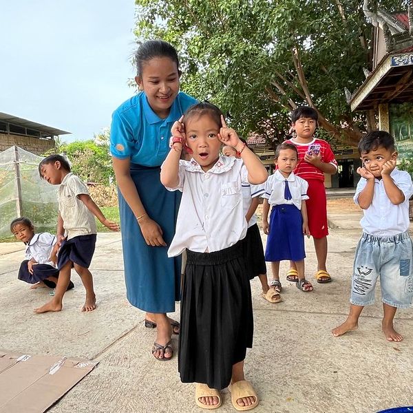 A TukTuk staff member smiles as children play and strike funny poses in a school yard