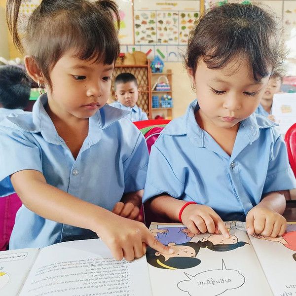 Two girls in school uniform point at the pictures in a TukTuk storybook in their classroom