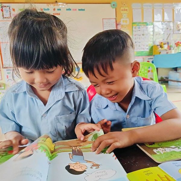 A girl and a boy laugh as they read a TukTuk picture book together in class