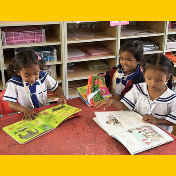 Three girls look through colourful picture books at a classroom table