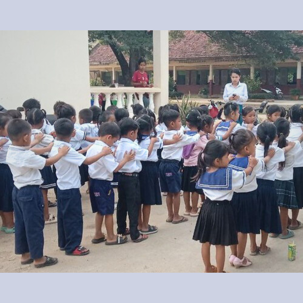 Preschool children stand in lines outdoors with their hands on each other's shoulders at school