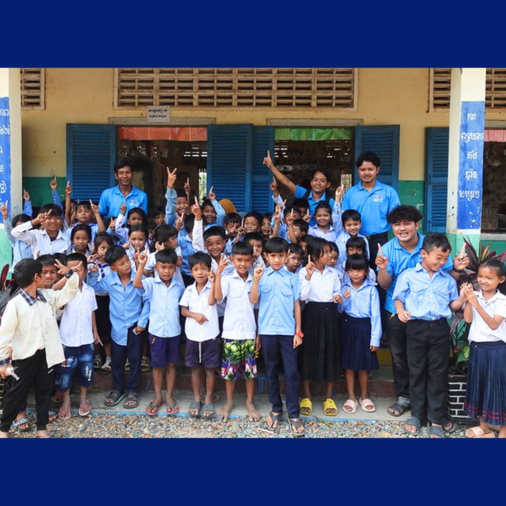TukTuk staff pose with a large group of children holding up their fingers outside their school