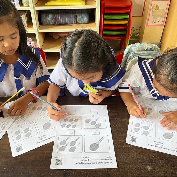 Three girls fill in counting worksheets with pencils at a classroom table