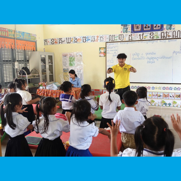 A TukTuk staff member leads an action song with preschool children in a classroom