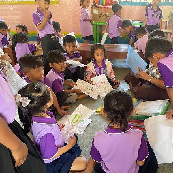 Preschool children in purple uniforms sit on the floor and work on activity worksheets