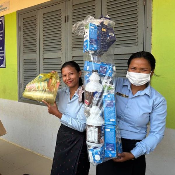 Two women hold up supplies wrapped in plastic outside a school classroom