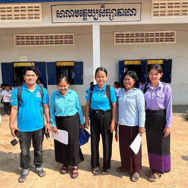 TukTuk staff and school staff pose together in front of a school building