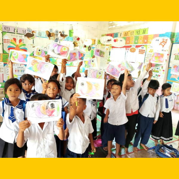 A class of preschool children hold up their coloured fish drawings in the classroom