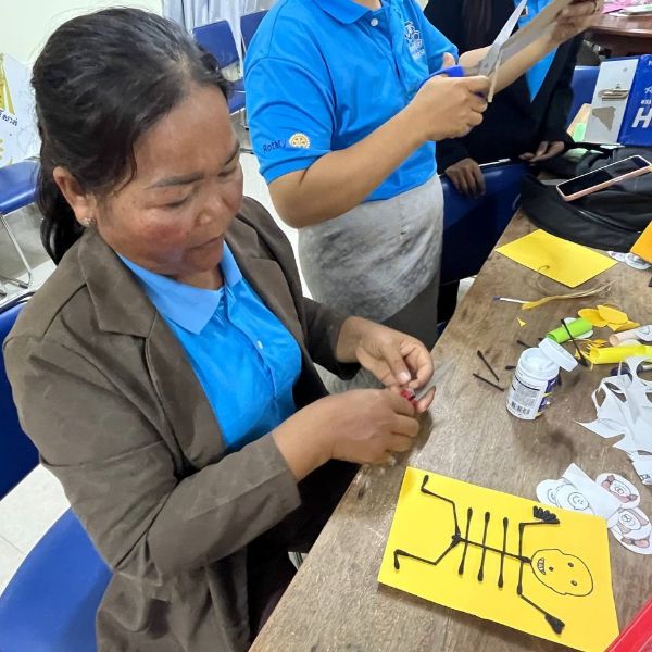 A teacher makes a skeleton craft from cotton buds on yellow paper at a workshop table